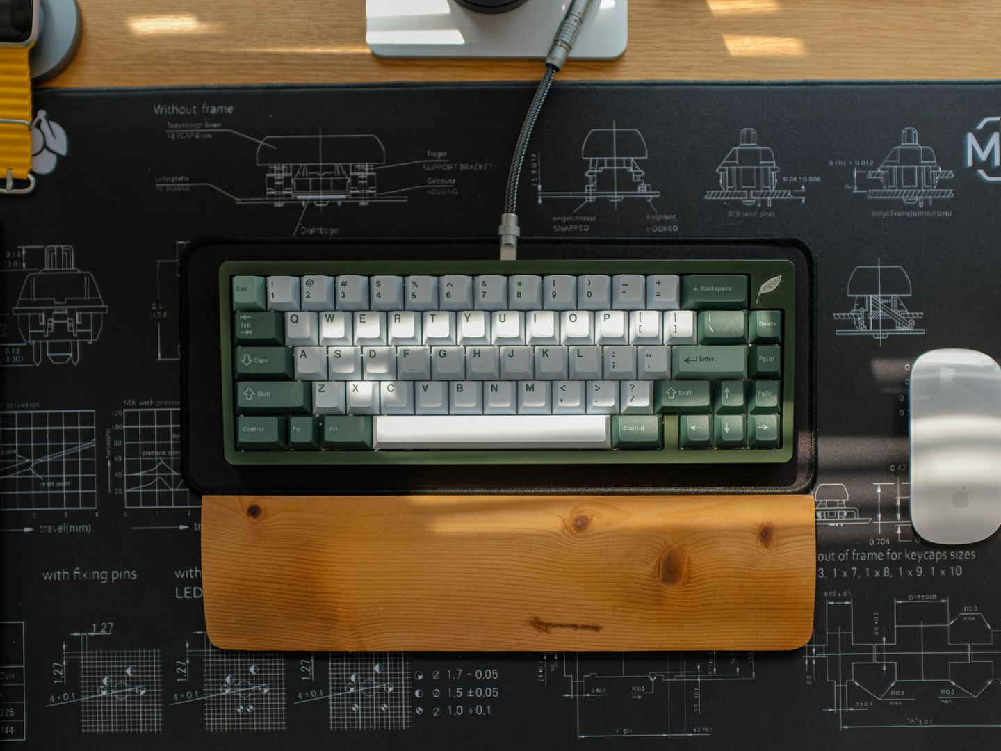 Top view of an ergonomic keyboard setup on a designer desk with a wooden wrist rest and blueprint themed mouse pad.